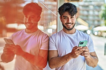 Young hispanic man smiling confident using smartphone at street