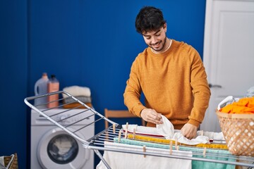 Young hispanic man smiling confident hanging clothes on clothesline at laundry room