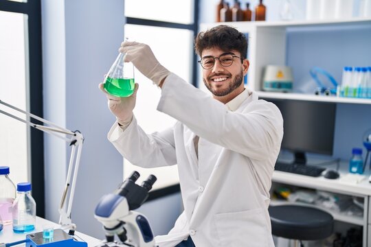 Young hispanic man scientist smiling confident measuring liquid at laboratory - Powered by Adobe