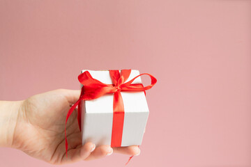 white gift box with red ribbon bow in woman hand with white sweater with copy space.