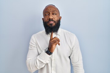 African american man standing over blue background thinking concentrated about doubt with finger on chin and looking up wondering