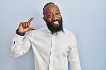 African american man standing over blue background smiling and confident gesturing with hand doing small size sign with fingers looking and the camera. measure concept.
