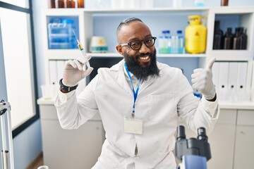 African american man working at scientist laboratory holding syringe smiling happy and positive, thumb up doing excellent and approval sign