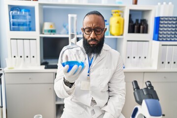 Young african american man wearing scientist uniform holding test tube at laboratory