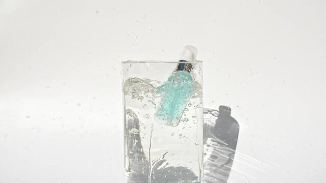 Cosmetic bottle, vial for oil, liquid, collagen serum falling down in water and splashes on white background. Slow motion. Women's cosmetics skincare. Sample of layout of package beauty product.FullHD