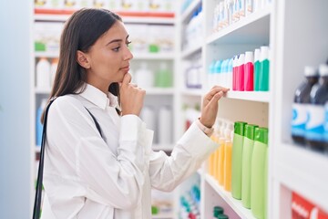 Young beautiful hispanic woman client holding toothpaste at pharmacy