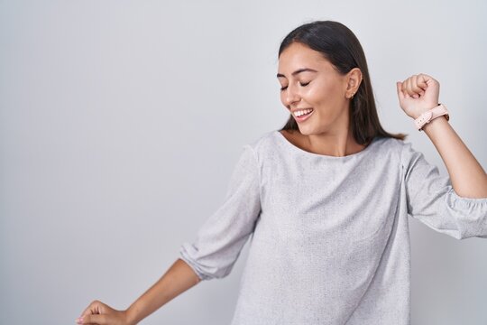 Young hispanic woman standing over white background dancing happy and cheerful, smiling moving casual and confident listening to music