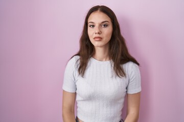 Obraz premium Young hispanic girl standing over pink background relaxed with serious expression on face. simple and natural looking at the camera.