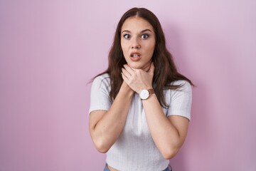 Young hispanic girl standing over pink background shouting suffocate because painful strangle....