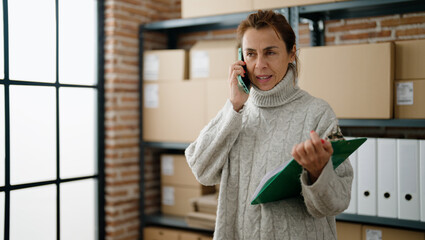 Middle age hispanic woman ecommerce business worker talking on the smartphone at storehouse office