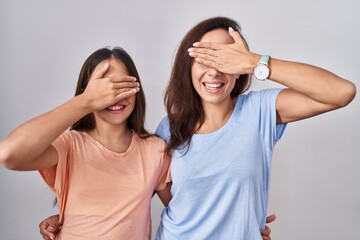 Fototapeta na wymiar Young mother and daughter standing over white background smiling and laughing with hand on face covering eyes for surprise. blind concept.