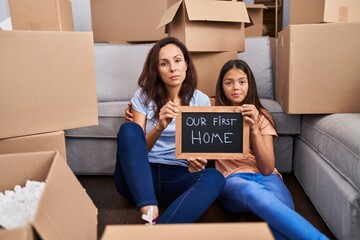 Young mother and daughter sitting on the floor at new home relaxed with serious expression on face....