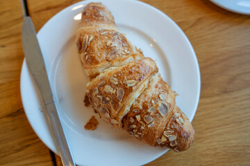 a plate with a almond croissant and knife on a table in a cafe.  View from above.