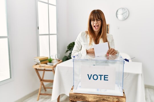 Hispanic business woman voting putting envelop in ballot box sticking tongue out happy with funny expression. emotion concept.