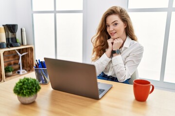 Young caucasian woman working at the office using computer laptop laughing nervous and excited with...