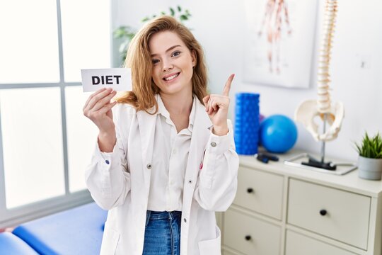 Young caucasian woman working at rehabilitation clinic holding diet banner smiling happy pointing with hand and finger to the side