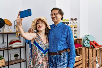 Middle age man and woman smiling confident make selfie by the smartphone at clothing store