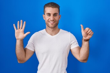 Fototapeta premium Young caucasian man standing over blue background showing and pointing up with fingers number six while smiling confident and happy.
