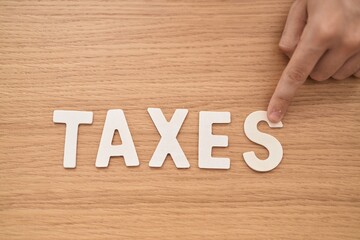 Young caucasian man business worker sitting on table pointing to taxes word at office