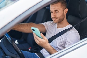 Young caucasian man using smartphone sitting on car at street