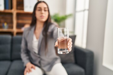 Young beautiful hispanic woman psychologist offering glass of water at psychology clinic