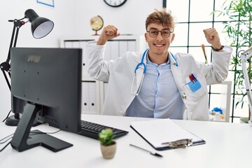 Young caucasian doctor man working at the clinic showing arms muscles smiling proud. fitness concept.