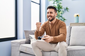 Young hispanic man playing video game sitting on sofa at home