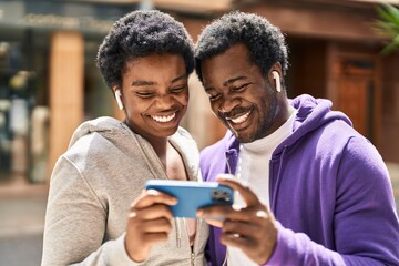 African american man and woman couple watching video on smartphone at street