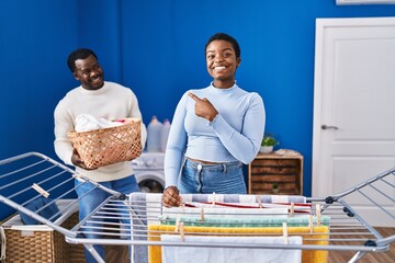 Young african american couple hanging clothes at clothesline smiling happy pointing with hand and finger