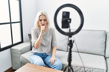 Young caucasian woman recording vlog tutorial with smartphone at home feeling unwell and coughing...