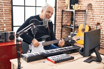 Middle age grey-haired man musician singing song playing electrical guitar at music studio