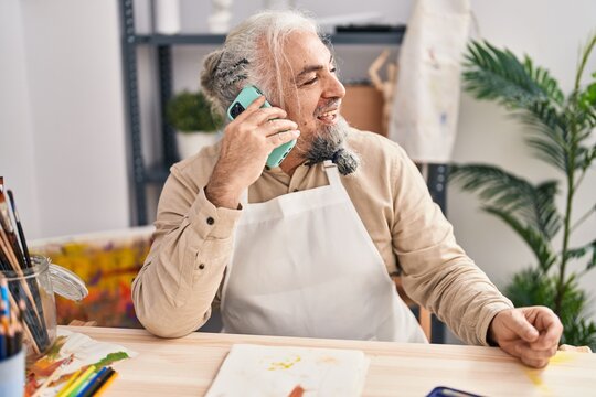 Middle age grey-haired man artist smiling confident talking on smartphone at art studio