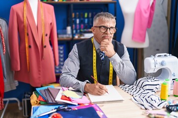 Middle age grey-haired man tailor drawing on notebook at clothing factory