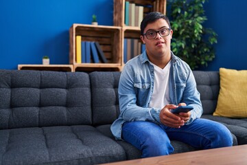 Down syndrome man using smartphone sitting on sofa at home