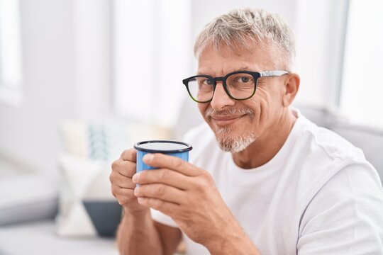 Middle age grey-haired man drinking coffee sitting on sofa at home