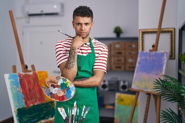 Brazilian young man holding painter palette at artist studio skeptic and nervous, frowning upset because of problem. negative person.