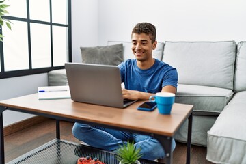 Young hispanic man using laptop sitting on the floor at home