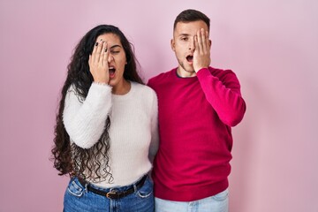 Naklejka premium Young hispanic couple standing over pink background yawning tired covering half face, eye and mouth with hand. face hurts in pain.