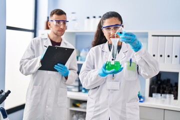 Man and woman wearing scientist uniform write on document measuring liquid at laboratory