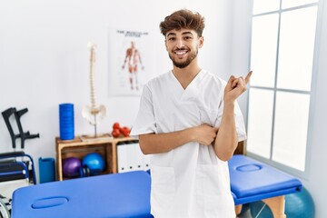 Obraz premium Young arab man working at pain recovery clinic with a big smile on face, pointing with hand and finger to the side looking at the camera.