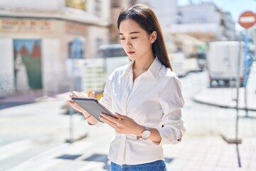 Young chinese woman using touchpad with serious expression at street