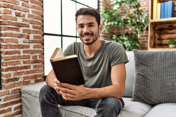 Young hispanic man smiling confident reading book at home