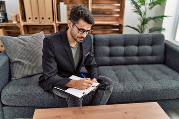 Young hispanic man having psychology session writing on checklist at clinic