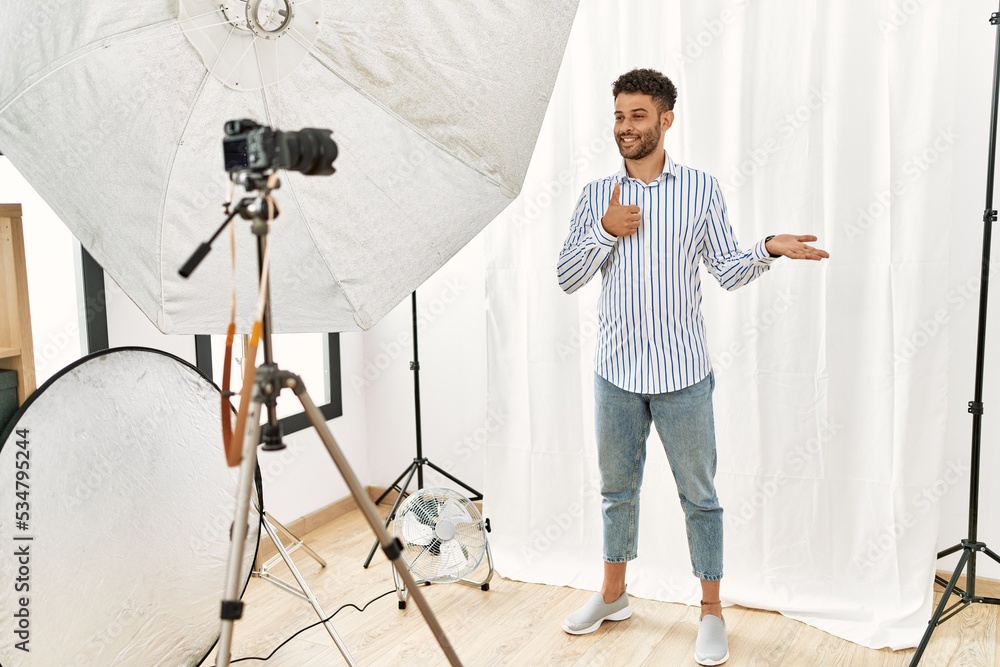 Sticker Arab young man posing as model at photography studio showing palm hand and doing ok gesture with thumbs up, smiling happy and cheerful