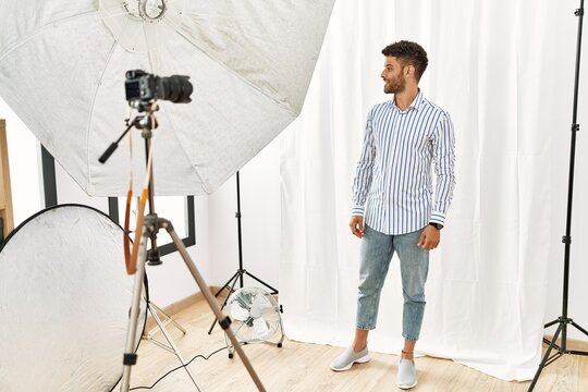 Arab young man posing as model at photography studio looking away to side with smile on face, natural expression. laughing confident.