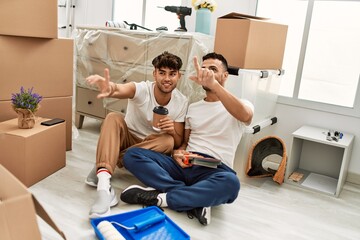 Two hispanic men couple drinking coffee choosing wall color at new home