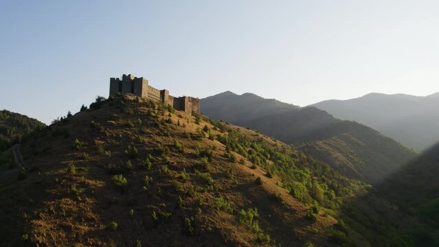 Medieval fortress Maglic on a hill at sunrise with a descending drone shot and moving away from the fortress, edited with only minimal color correction