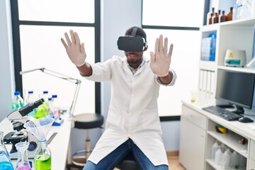 Fototapeta na wymiar Young african american man wearing scientist uniform using virtual reality glasses at laboratory