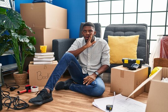 African american man sitting on the floor at new home hand on mouth telling secret rumor, whispering malicious talk conversation