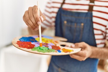 Young hispanic man mixing color on palette at art studio